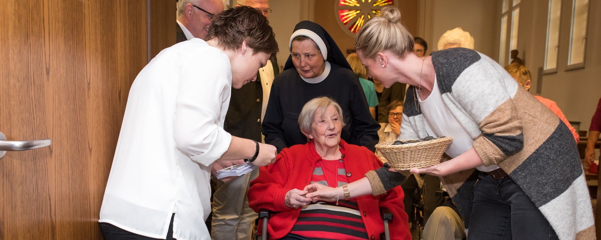 Nach der Messe: eine Ordensschwester schiebt eine Frau im Rollstuhl aus der Kirche