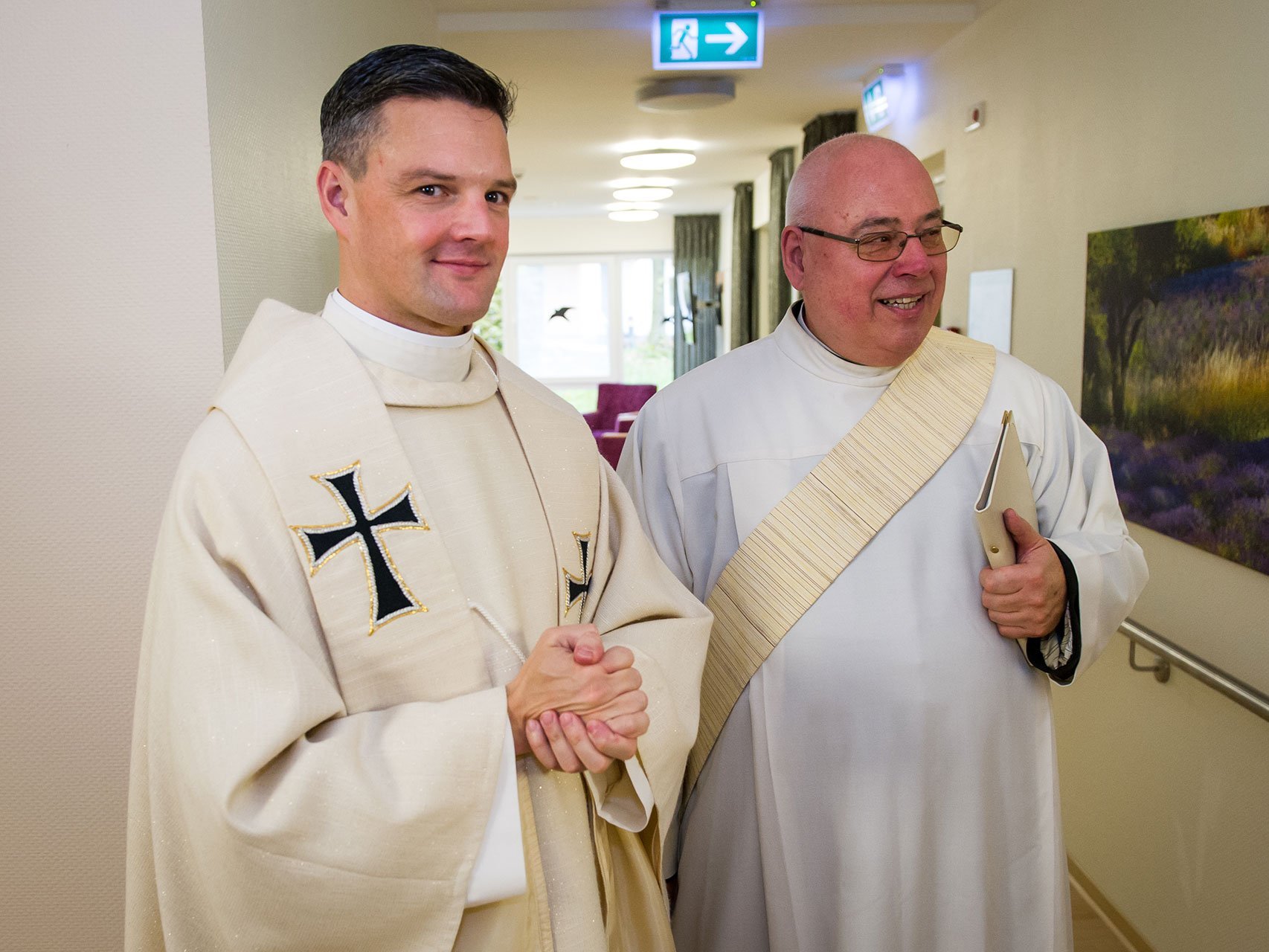 Pater Jörg blickt in die Kamera, während ein weiterer Pater sich mit jemanden zu unterhalten scheint