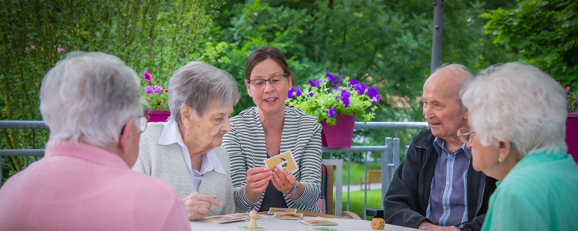 Eine Pflegerin unterstützt Bewohner/innen beim Kartenspiel auf der Terasse