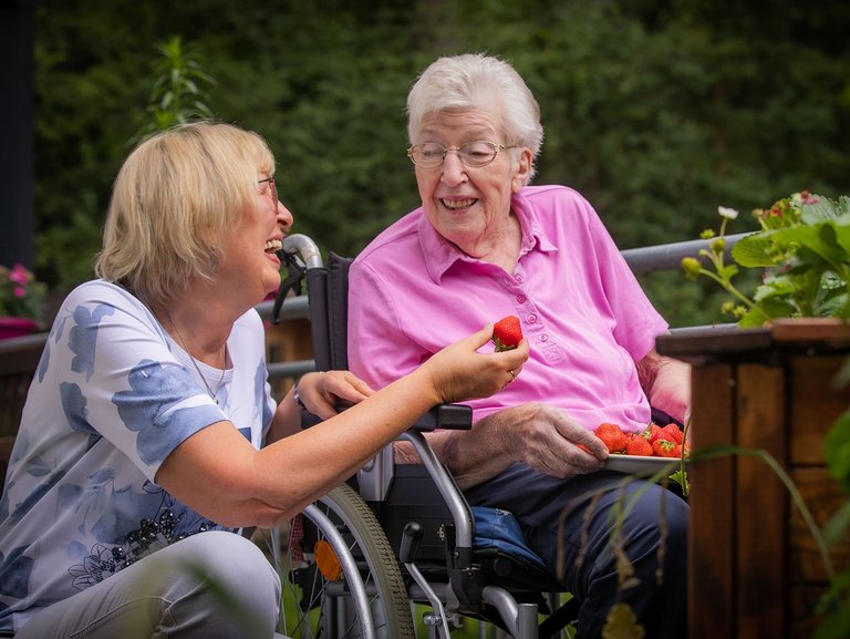 Zwei Frauen lachen und essen Erdbeeren auf der Terasse